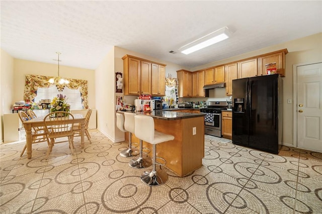 kitchen with a notable chandelier, under cabinet range hood, a peninsula, black fridge, and stainless steel gas stove