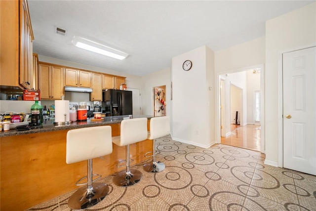 kitchen featuring a peninsula, a breakfast bar, visible vents, black fridge, and dark countertops