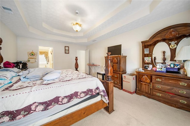 bedroom featuring light colored carpet, a tray ceiling, and visible vents