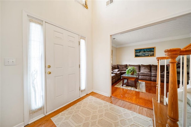 foyer entrance with a wealth of natural light, light wood-type flooring, visible vents, and crown molding