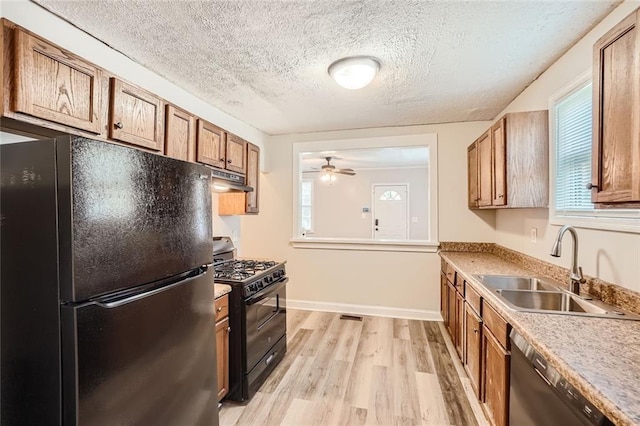 kitchen featuring brown cabinetry, light wood-style flooring, under cabinet range hood, black appliances, and a sink