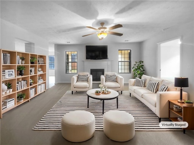 living area with a wealth of natural light, baseboards, a glass covered fireplace, and ceiling fan