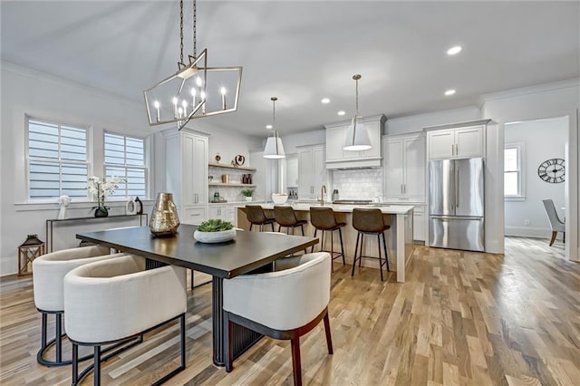 dining area with a chandelier, ornamental molding, light wood-type flooring, and a healthy amount of sunlight