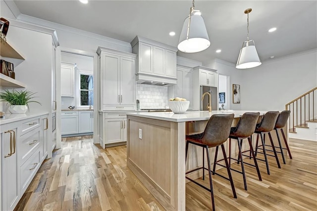 kitchen featuring decorative backsplash, a kitchen breakfast bar, a kitchen island with sink, pendant lighting, and white cabinetry