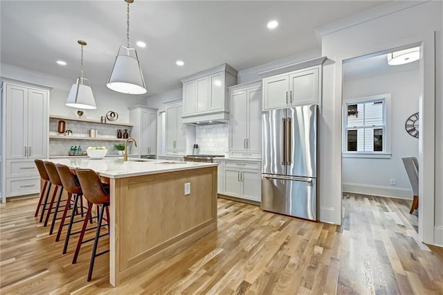 kitchen with white cabinetry, tasteful backsplash, high end refrigerator, an island with sink, and decorative light fixtures