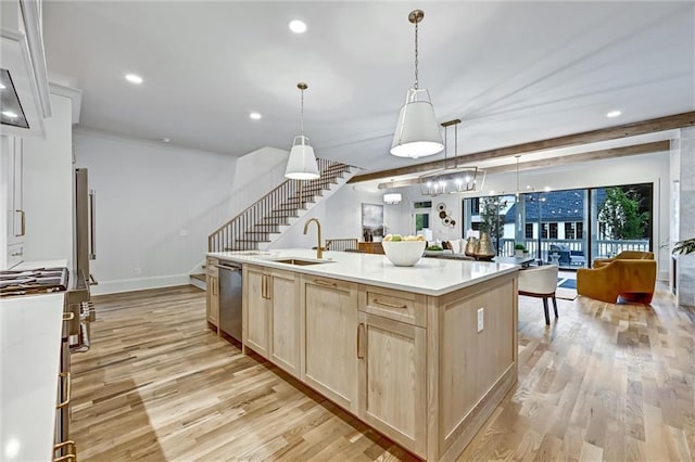 kitchen with stainless steel dishwasher, sink, decorative light fixtures, light hardwood / wood-style flooring, and a center island with sink