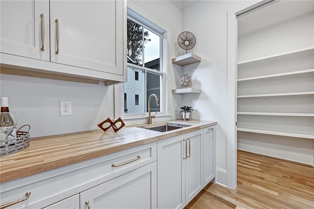 kitchen featuring light wood-type flooring, white cabinetry, butcher block counters, and sink