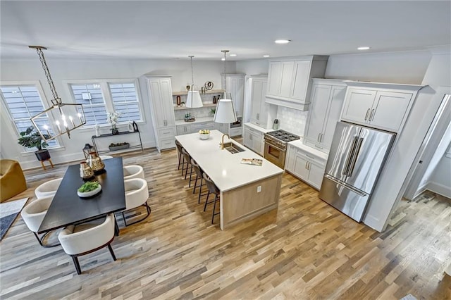 kitchen featuring appliances with stainless steel finishes, backsplash, a kitchen island with sink, pendant lighting, and white cabinetry