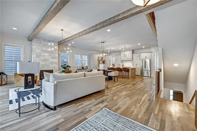 living room featuring beam ceiling, light hardwood / wood-style flooring, and an inviting chandelier