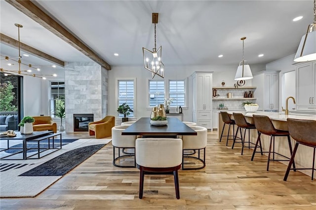 dining space featuring sink, beam ceiling, an inviting chandelier, a fireplace, and light hardwood / wood-style floors