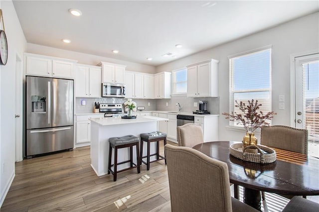 kitchen featuring a center island, a kitchen breakfast bar, white cabinetry, wood-type flooring, and stainless steel appliances