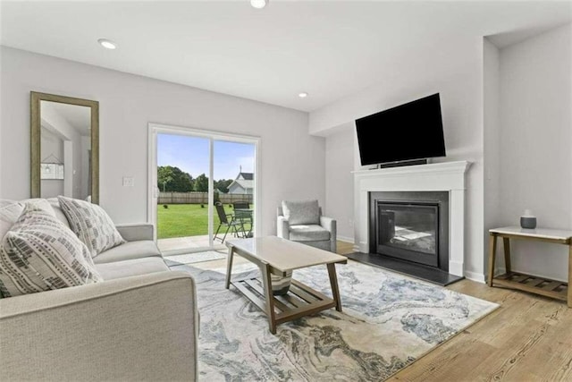 living area featuring baseboards, a glass covered fireplace, light wood-style flooring, and recessed lighting