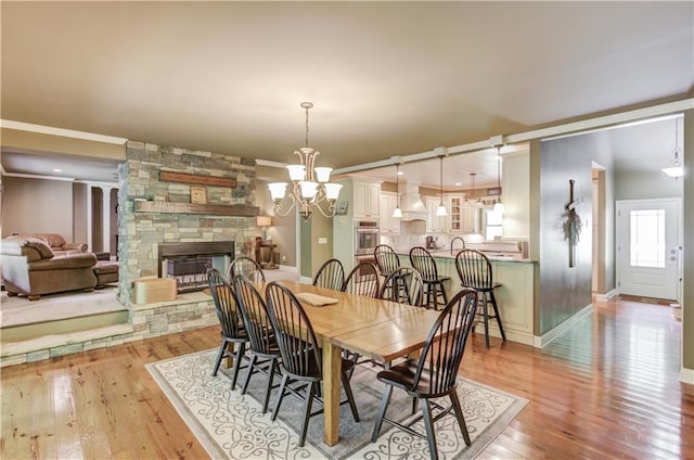 dining space with crown molding, a notable chandelier, a stone fireplace, and light hardwood / wood-style floors