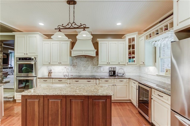 kitchen featuring appliances with stainless steel finishes, light stone counters, a kitchen island, decorative light fixtures, and beverage cooler