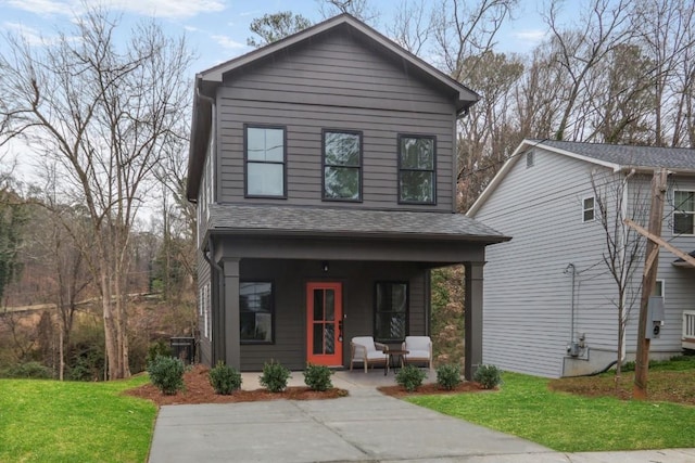 traditional-style home featuring roof with shingles, covered porch, and a front yard