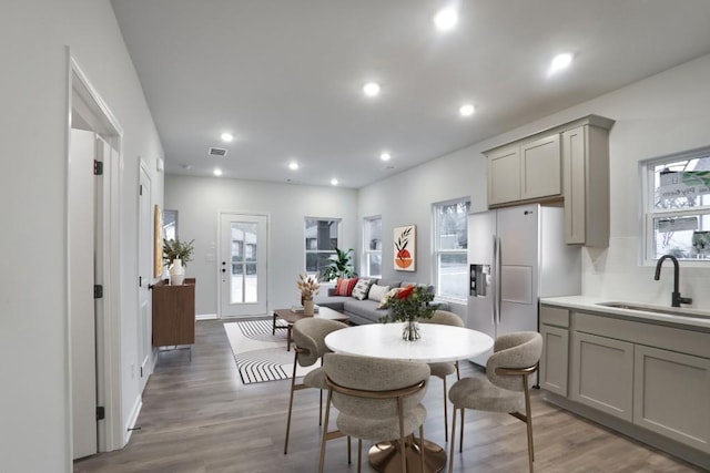 kitchen featuring wood finished floors, recessed lighting, gray cabinets, a sink, and fridge with ice dispenser