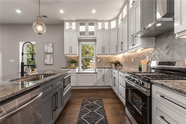 kitchen featuring stainless steel appliances, sink, white cabinetry, light stone counters, and wall chimney range hood