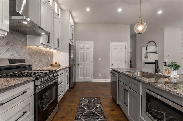 kitchen with stainless steel appliances, light stone countertops, wall chimney exhaust hood, white cabinets, and sink