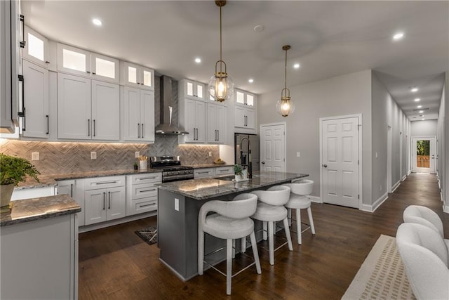 kitchen with appliances with stainless steel finishes, an island with sink, wall chimney range hood, and white cabinetry