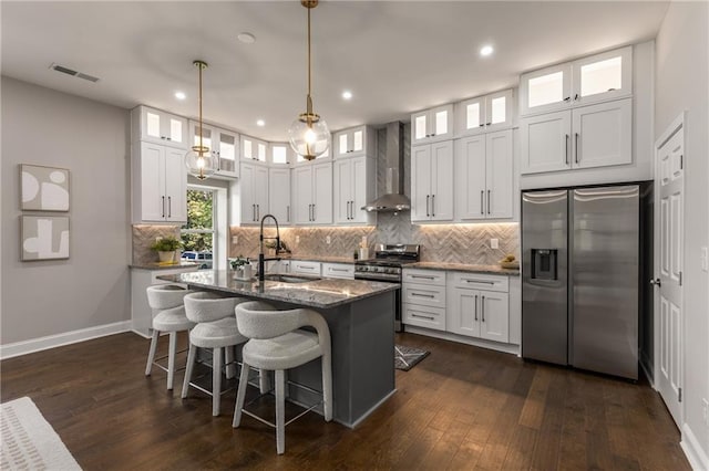 kitchen featuring stainless steel appliances, an island with sink, sink, white cabinetry, and wall chimney range hood