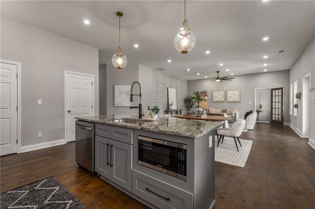 kitchen featuring stainless steel appliances, decorative light fixtures, ceiling fan, gray cabinets, and a kitchen island with sink