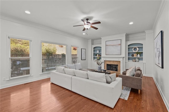 living room with wood-type flooring, ornamental molding, ceiling fan, and built in shelves