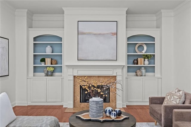 living room featuring hardwood / wood-style flooring, a premium fireplace, built in features, and crown molding