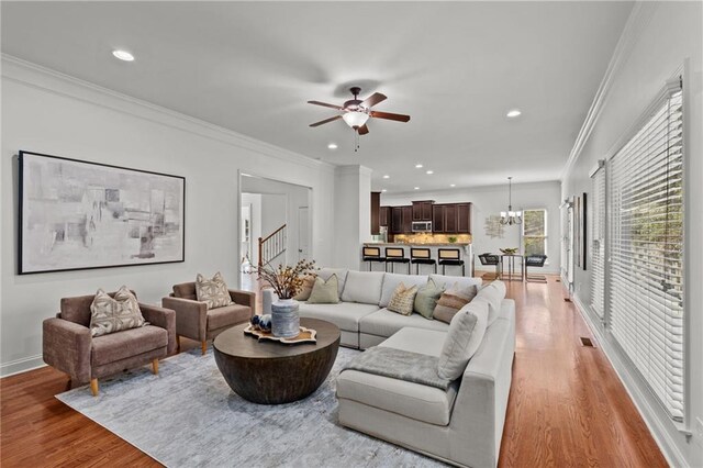 living room with crown molding, ceiling fan with notable chandelier, and light wood-type flooring