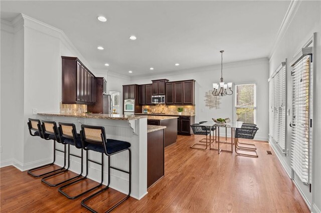 kitchen with appliances with stainless steel finishes, ornamental molding, decorative light fixtures, kitchen peninsula, and light wood-type flooring