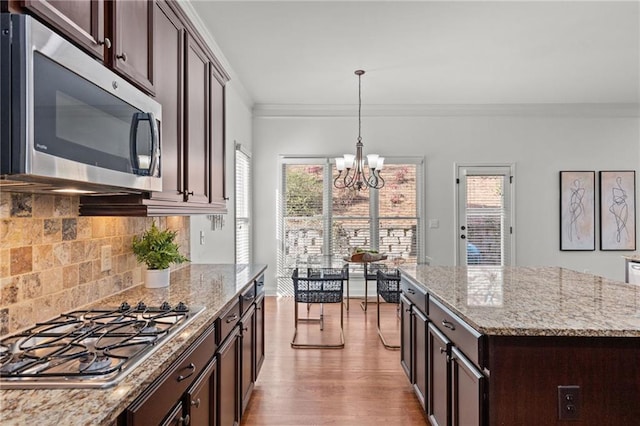 kitchen with crown molding, dark brown cabinetry, stainless steel appliances, and light stone countertops