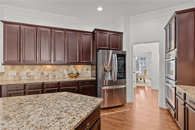 kitchen featuring crown molding, stainless steel appliances, tasteful backsplash, light stone countertops, and light wood-type flooring