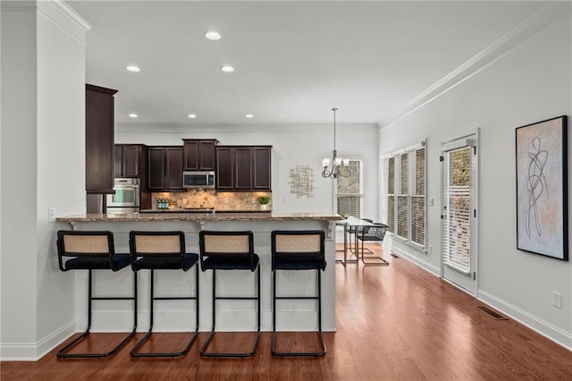 kitchen with a breakfast bar area, decorative light fixtures, appliances with stainless steel finishes, kitchen peninsula, and backsplash