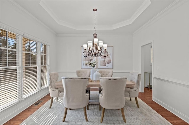 dining area with ornamental molding, wood-type flooring, a raised ceiling, and a notable chandelier