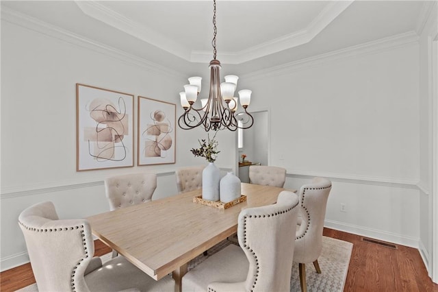 dining room with ornamental molding, dark hardwood / wood-style floors, an inviting chandelier, and a tray ceiling