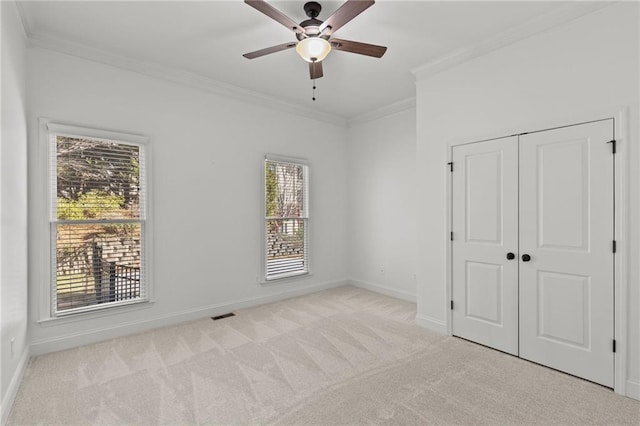 unfurnished bedroom with crown molding, light colored carpet, a closet, and ceiling fan