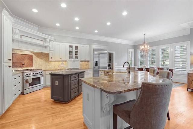 kitchen featuring a kitchen bar, a kitchen island with sink, pendant lighting, high quality appliances, and white cabinets