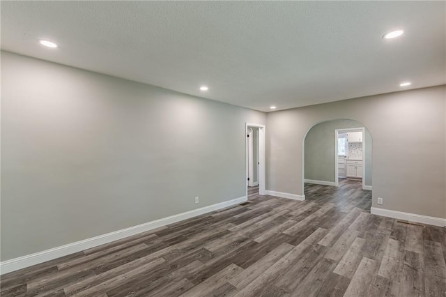 unfurnished room featuring recessed lighting, arched walkways, dark wood-style flooring, and baseboards