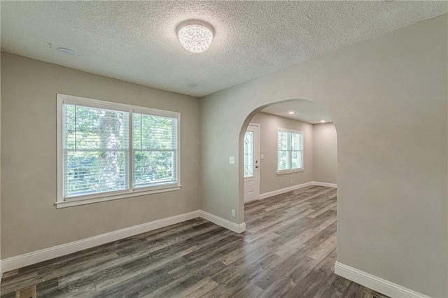 foyer entrance featuring baseboards, dark wood-style floors, arched walkways, and a textured ceiling