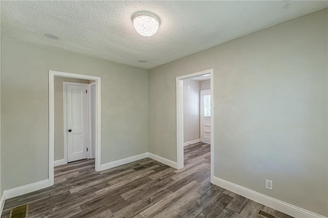 unfurnished room featuring visible vents, baseboards, dark wood-style floors, and a textured ceiling