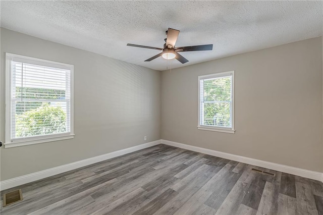 spare room featuring baseboards, wood finished floors, visible vents, and a textured ceiling