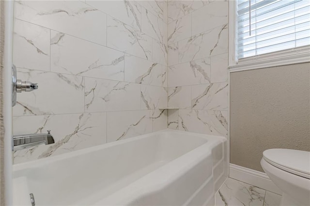 bathroom featuring marble finish floor, a textured wall, toilet, and baseboards