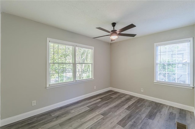 spare room featuring wood finished floors, visible vents, baseboards, a textured ceiling, and ceiling fan