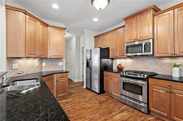 kitchen featuring sink, dark stone countertops, stainless steel appliances, dark hardwood / wood-style floors, and decorative backsplash