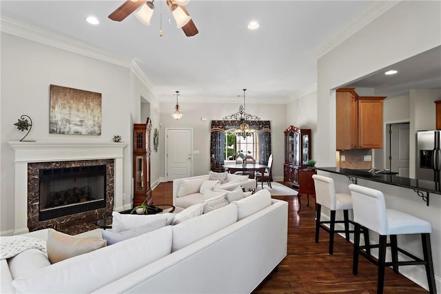 living room with ceiling fan with notable chandelier, ornamental molding, dark hardwood / wood-style flooring, and a premium fireplace