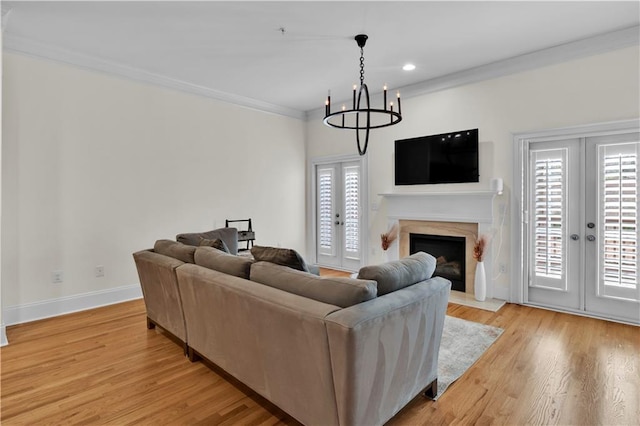 living area featuring light wood-style floors, french doors, a notable chandelier, and baseboards