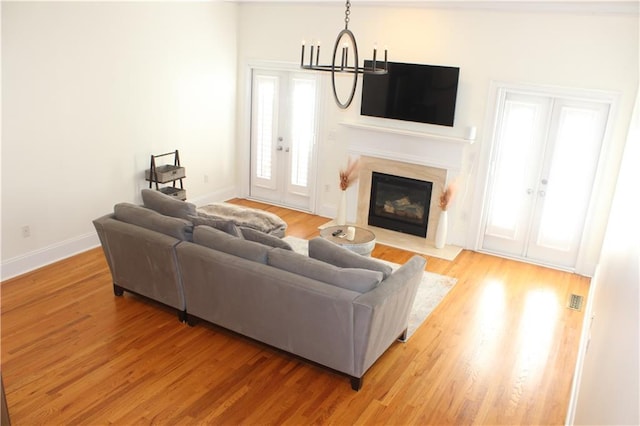 living area with baseboards, an inviting chandelier, french doors, light wood-style floors, and a fireplace