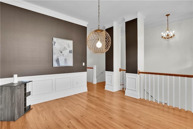 spare room featuring ornamental molding, a wainscoted wall, light wood-style floors, and a notable chandelier