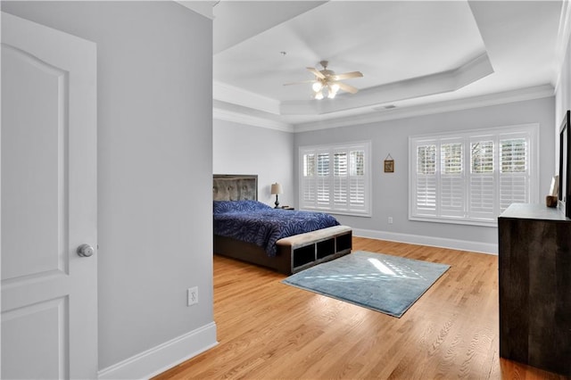 bedroom with light wood-type flooring, a tray ceiling, and multiple windows