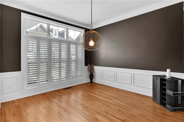 unfurnished dining area with a wainscoted wall, crown molding, visible vents, and wood finished floors