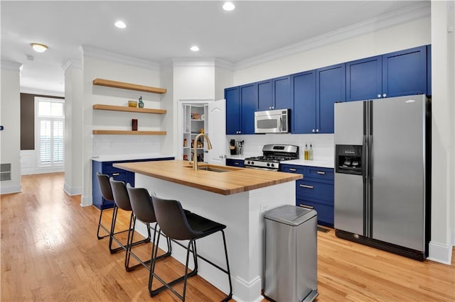 kitchen featuring butcher block countertops, appliances with stainless steel finishes, blue cabinetry, a kitchen bar, and a sink